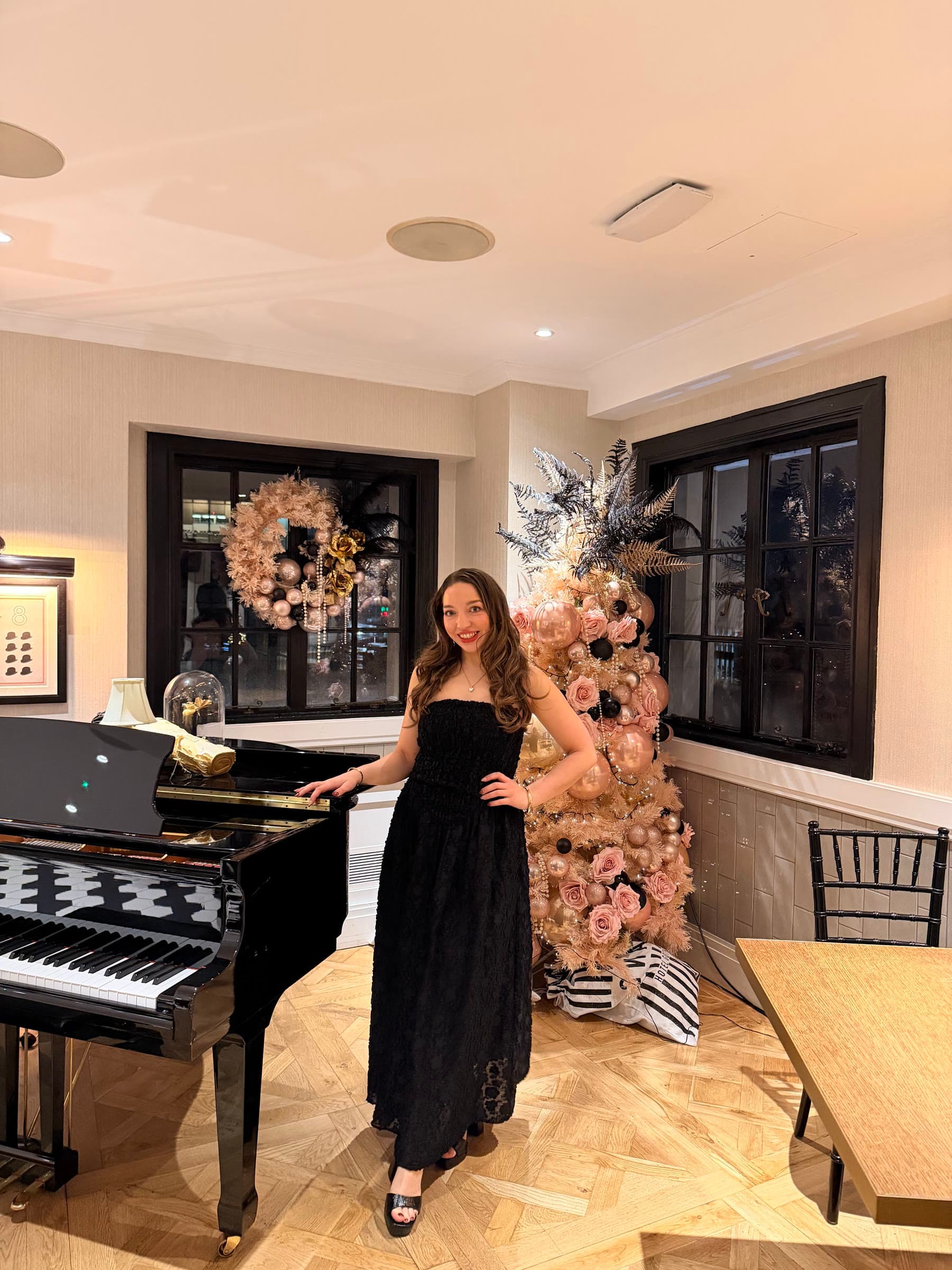 Olivia in a black dress beside a grand piano and a pink Christmas tree