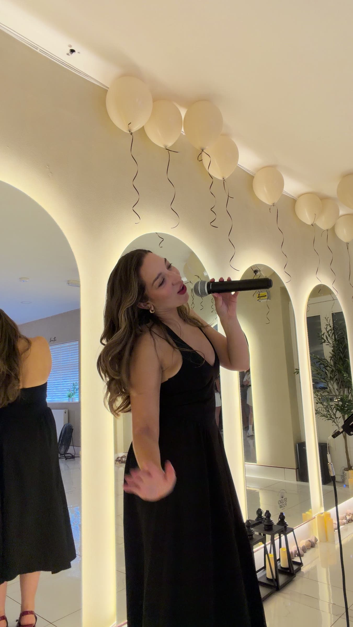 Olivia singing at a party under white balloons, in a black dress