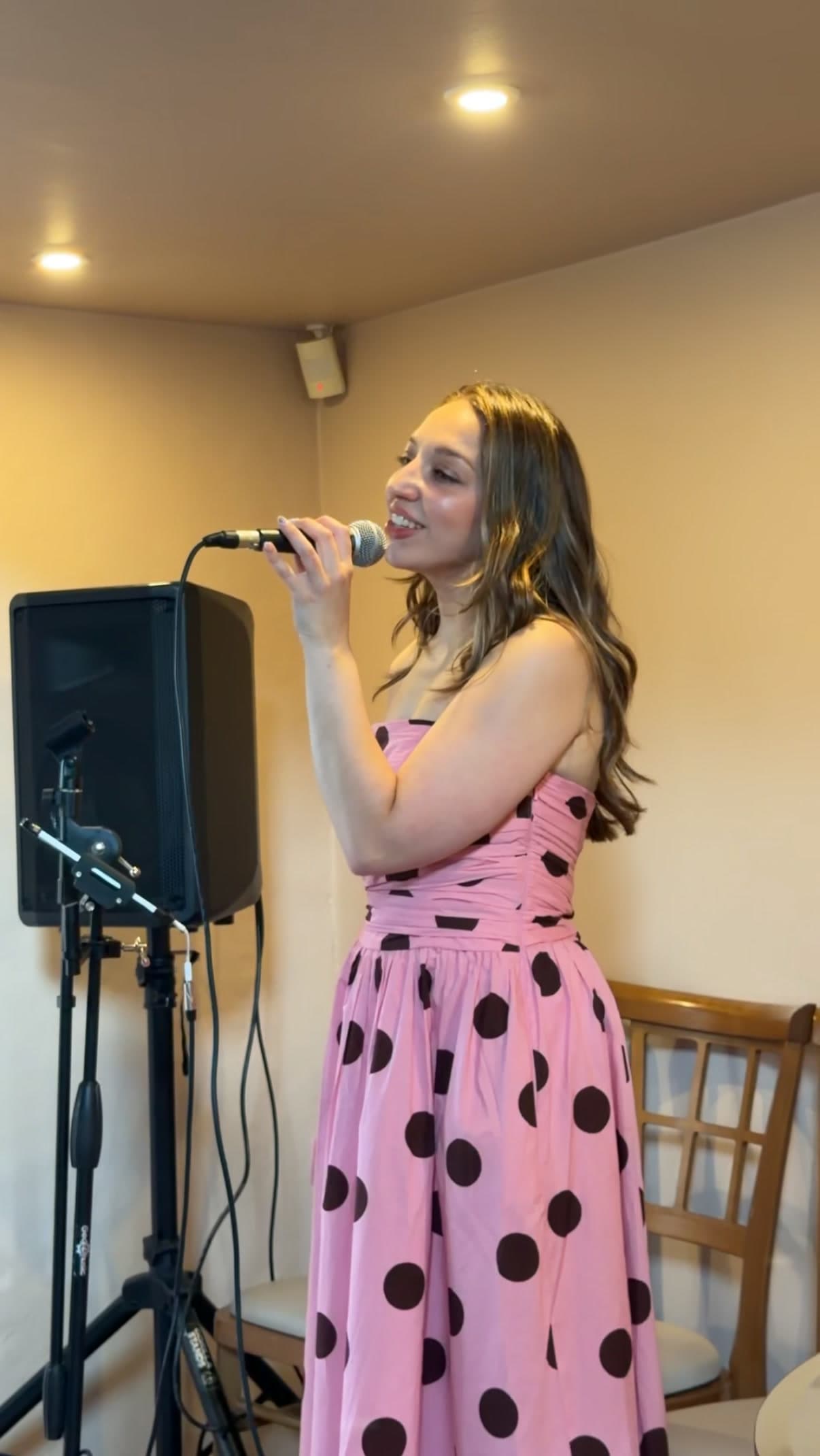 Olivia singing into a microphone in a pink polka-dot dress
