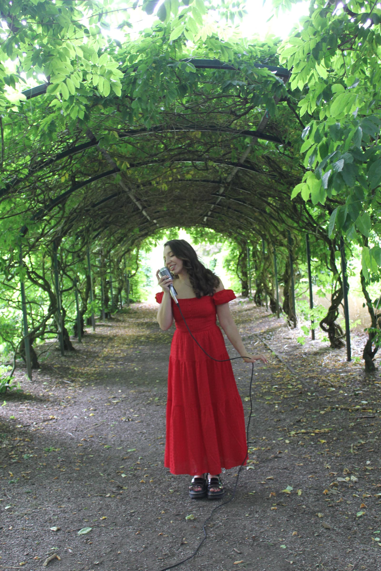 Olivia singing beneath a leafy garden archway in a red dress