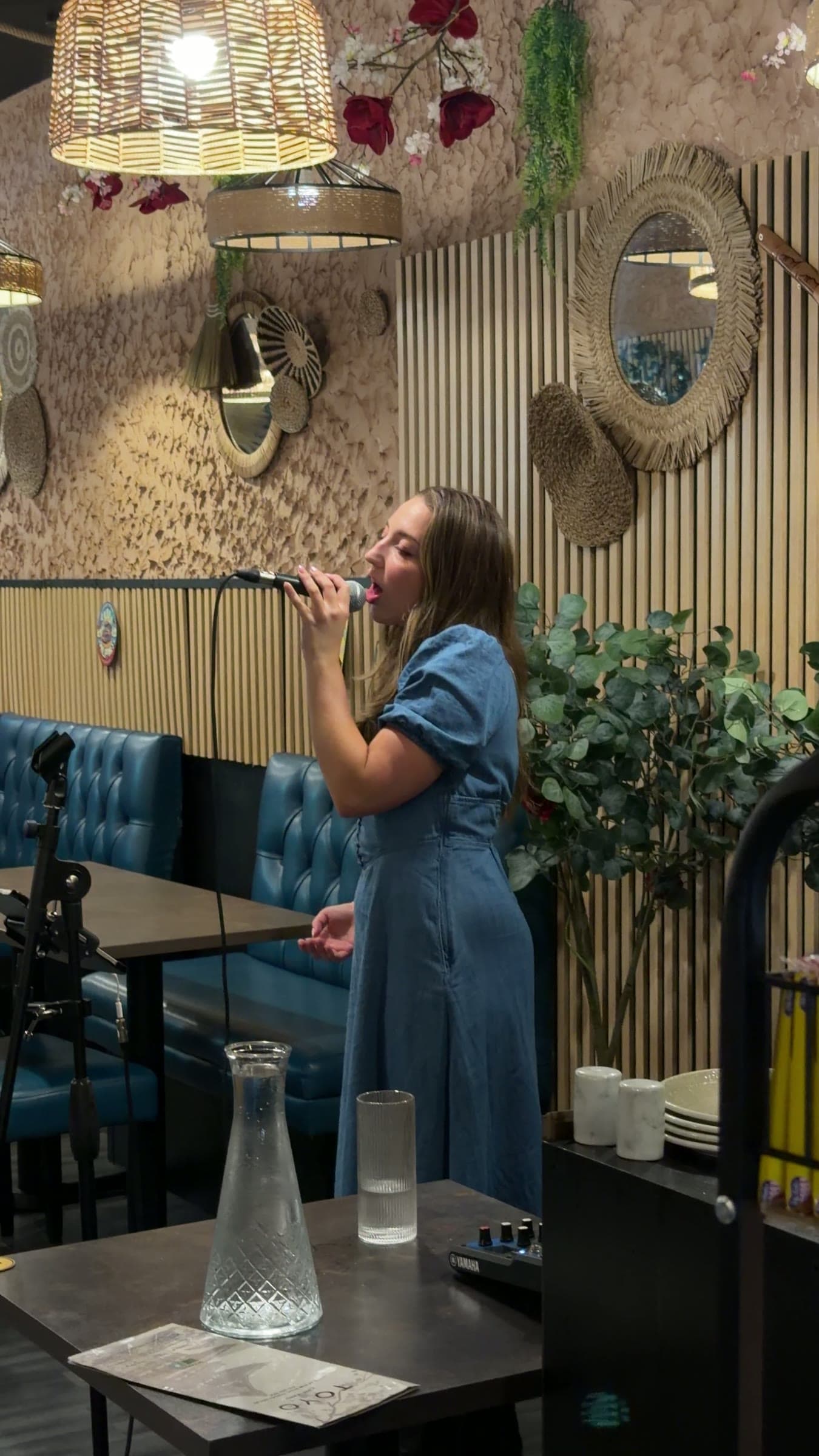 Olivia singing to diners in a restaurant, in a blue dress