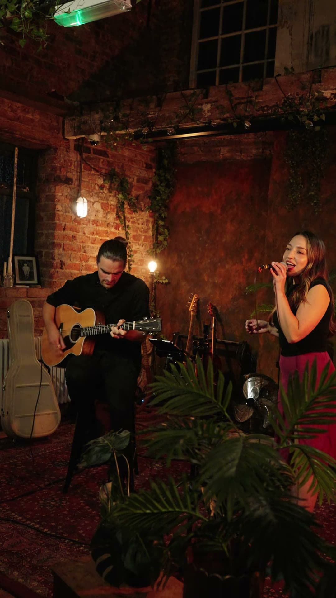 Olivia singing with Danny on acoustic guitar in a candlelit brick bar